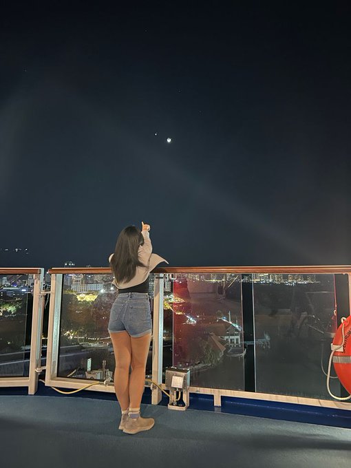 The image features a woman standing on a balcony, looking up at the sky with a telescope pointed towards the moon. She appears to be enjoying her time observing celestial objects. The photo also includes an overlay of a city skyline, which adds depth to the scene. The caption for the image reads "good night Web3 good night @Polymarket good night @base good night @wallchain good night @NomismaNetwork Creator Active".