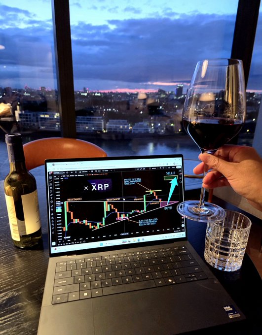 A person toasts with a glass of red wine while a laptop displays an XRP breakout chart, set against a stunning dusk cityscape view over the water—perfectly capturing the "Europe vacation" crypto trading vibe described in the post.