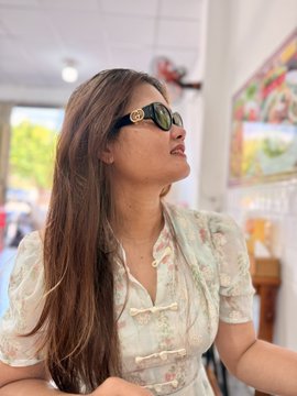 A young woman with long straight hair wearing a floral pastel top and Gucci sunglasses, posing indoors with her face tilted upward.