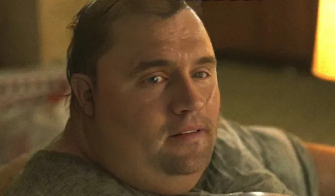 A man with slicked-back hair wearing a gray shirt looks up with a skeptical, side-eye expression in a dimly lit room. The image humorously illustrates the post's point about Solana traders' contradictory behavior—hypocritically criticizing the chain while benefiting from its gains, much like the man's "wait, really?" expression conveys disbelief at the hypocrisy described.