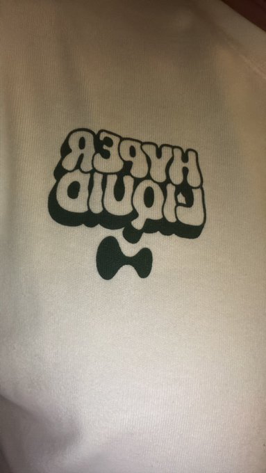A cream-colored t-shirt or tote bag features dark green bubble-letter text stacked in two rows above a bow-tie-shaped graphic that mimics the AISC pool logo.