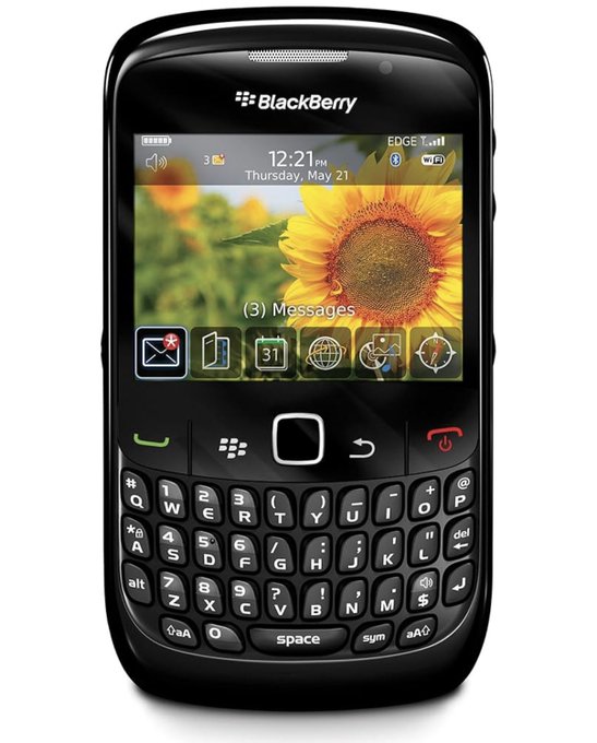 A black BlackBerry smartphone displaying a sunflower wallpaper, showing the time 12:21 PM on Thursday, May 21, with (3) Messages notification and various app icons on the home screen.
