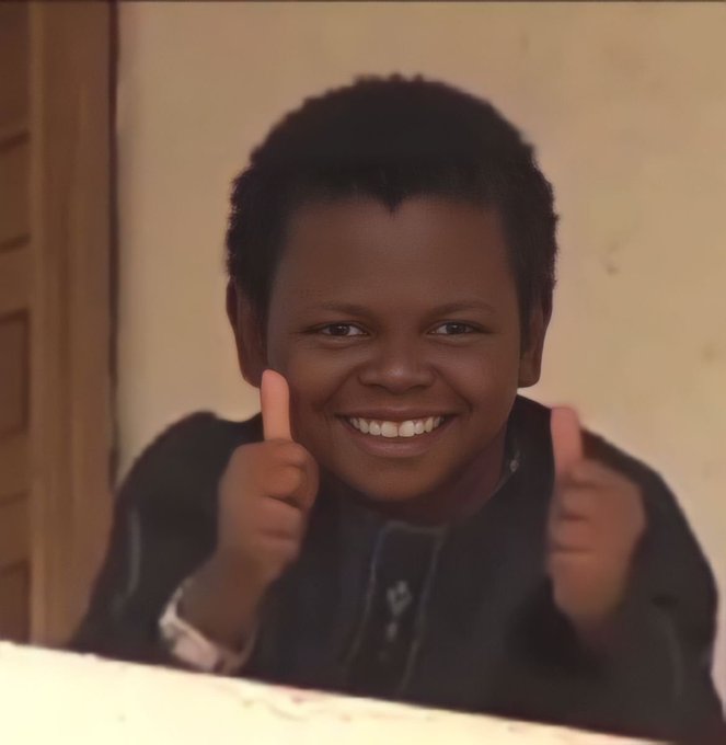 A young boy with a big smile gives two thumbs up while looking directly at the camera.