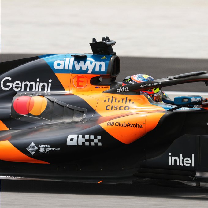 A close-up of a McLaren Formula 1 car in its orange, black, and blue livery, featuring sponsor logos including "allwyn," "Gemini," "Cisco," "Club Avolta," "OKX," "intel," "Mastercard," and "Bahrain International Circuit," with the driver's helmet labeled "Iron Mountain" visible in the cockpit. The "allwyn" branding directly ties into the post's "New Money App" message, highlighting Allwyn's sponsorship presence in the high-profile Singapore Grand Prix setting.