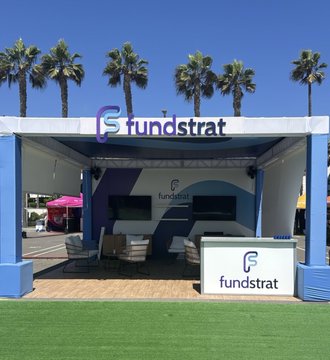 A "Fundstrat" branded outdoor booth set up with palm trees and modern seating in the background, welcoming visitors to Future Proof in Huntington Beach. The setup reflects Fundstrat's presence at the event, as highlighted by the tagged partners and tickers in the post.