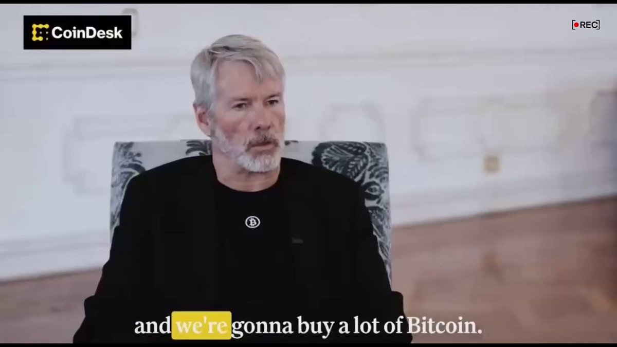 The image features a man sitting in a chair, wearing a black shirt with white lettering. The text "MICHAEL SAYLOR JUST SAID BITCOIN IS GOING TO GO BACK INTO A SERIOUS BULL MARKET" is displayed above him, and another piece of text below the man reads: "THIS IS VERY BULLISH". This suggests that Michael Saylors has made a statement about Bitcoin being bullish or going back into a serious bull market.

The image also includes some text in the bottom right corner stating "we're gonna buy a lot of Bitcoin." The overall context seems to be related to cryptocurrency, with the man's statement potentially referring to Bitcoin specifically.