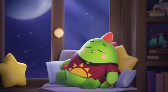 A 3D animated scene shows a round green character wearing a red shirt with a sun emblem, sleeping on a pillow next to a window at night.