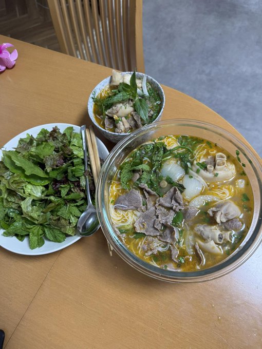 A bowl of Vietnamese beef pho with fresh herbs and a side plate of greens sits on a wooden table. The accompanying post about Ukraine moving $8.3M in seized USDT seems unrelated to the image, which simply depicts a meal.
