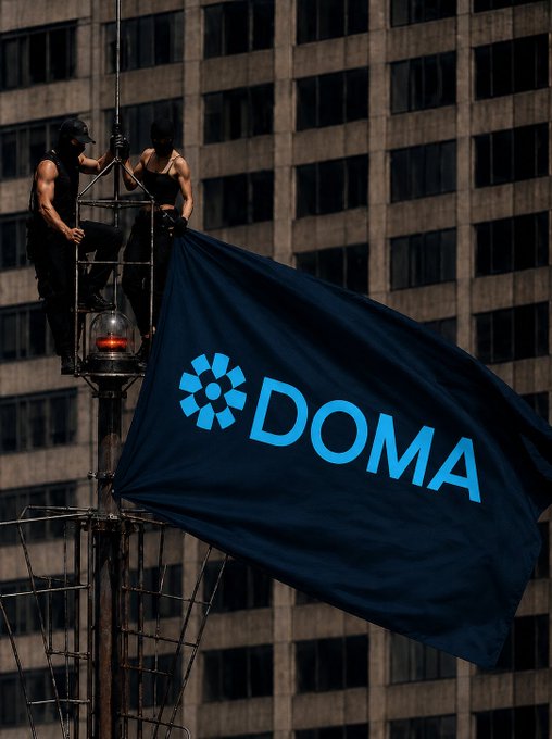 Two people dressed as Spider-Man climbing a tall antenna or tower, unfurling a dark blue flag with the logo and text 'DOMA' against a backdrop of a glass office building.