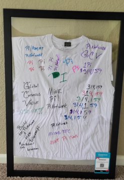 A framed white T-shirt signed by community members with their Pi usernames, Model numbers, and 3/14/159 dates (Pi Day), presented to Dr. Nicolas at Consensus 2026 as a symbol of the GCV community's support for Pi.