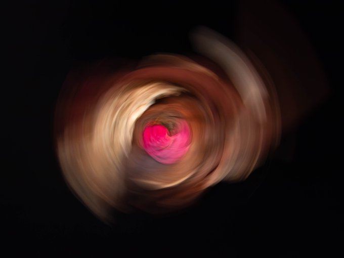A swirling spiral of motion-blurred brown and tan hues with a vibrant pink center creates an abstract, vortex-like photograph that complements the post's enthusiastic praise for photographer @AndrewHookerPh1's artistic work and their excitement about being "print 1" of his collection.