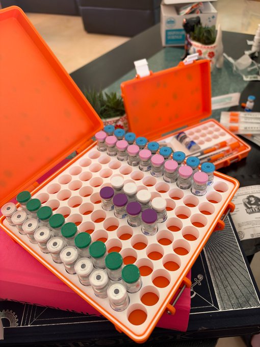 An open orange carrying case containing multiple vials organized by colored caps (green, white, pink, blue, and purple).