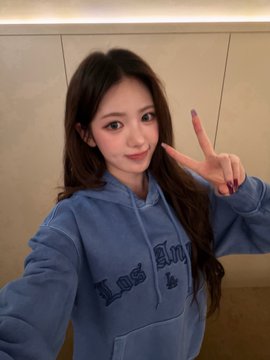 A selfie-style photo of a young woman in a blue 'Los Angeles' hoodie making a peace sign.