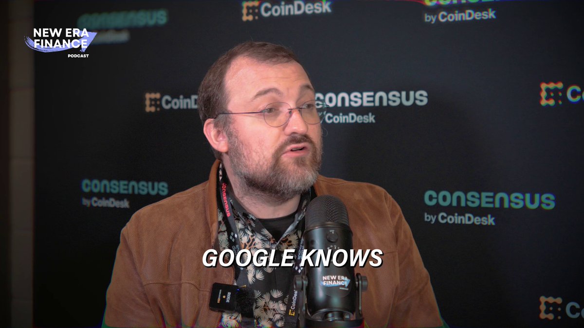 The image shows a man wearing glasses and a brown jacket speaking into a microphone at an event. The background features a black wall with logos for CoinDesk, Consensus, and Google Know. The man appears to be discussing something related to cryptocurrency or blockchain technology, possibly sharing insights about its future implications on the market.