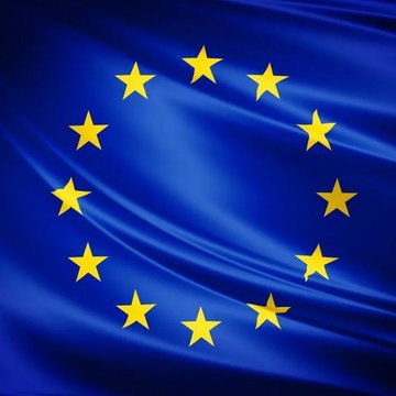 The European Union flag, featuring its iconic circle of twelve gold stars on a deep blue background, is displayed in a close-up shot with rippling fabric texture. The image accompanies news of the EU's 21st sanctions package against Russian banks, crypto platforms, and oil firms amid the ongoing war in Ukraine.
