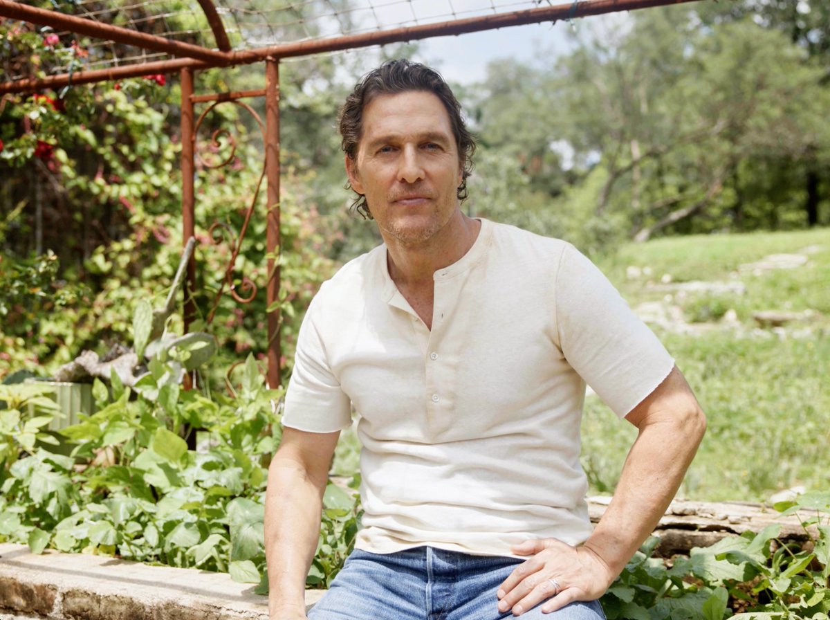Actor Matthew McConaughey sits outdoors in a cream henley shirt in a garden setting.