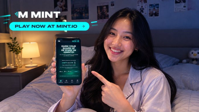A smiling young woman in pajamas sits on a bed pointing at her phone screen displaying "MINT" and "EARN YOUR SHARE OF $128K IN REWARDS," with "PLAY NOW AT MINT.IO" above.