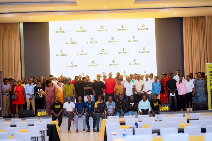 Attendees of the Binance Traders Bootcamp in Kigali gather for a group photo on stage in front of a large backdrop featuring the Binance logo, reflecting the event's focus on blockchain education, trading fundamentals, TradeFi, and BSTocks for the local community.