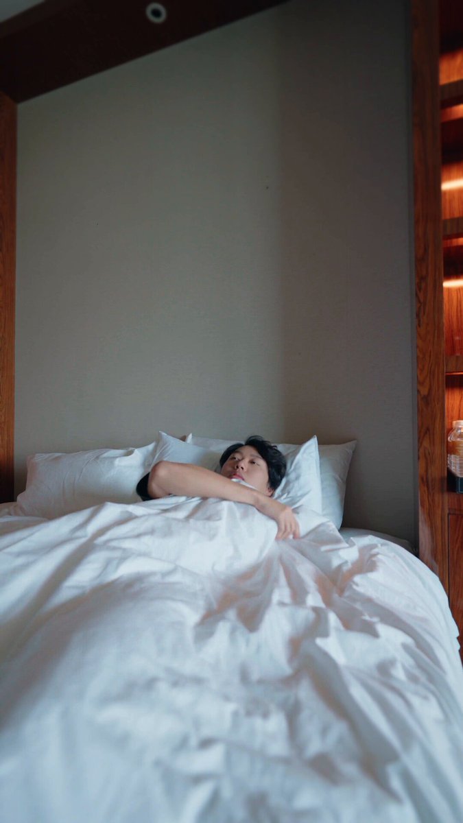 The image shows a person lying down on their bed with white sheets and pillows. The person appears to be resting or sleeping peacefully. The photo has been captioned, "For those we don' t know, I'm also an EXCELLENT engineer in @ThetanutsFi ... if you want to leverage options for your DeFi strategy, checkout our SDK!".