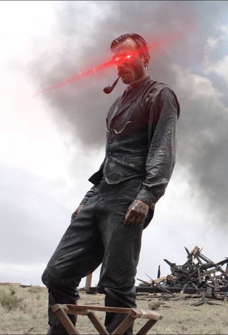 A man dressed in an old-fashioned dark suit smoking a pipe stands on a wooden stool in a desolate, smoky landscape, with red laser beams shooting from his eyes.