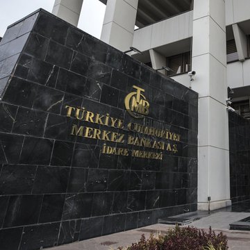 The image shows a large, black stone building with gold lettering that reads "Turkye Cevikirbanki Merkez Banka A." The building appears to be an important financial institution, but its exterior looks worn and aged due to the passage of time and the effects of weather. The surrounding area is filled with plants, adding a touch of nature to the scene. The image also contains text that reads "From the outside, it looks like a simple move worth 3 points. But no one is really talking about the true state of the banks on the inside. The credit taps are effectively shut off. Balance sheets are bloated under the pressure of high interest rates. With inflation over ın."
