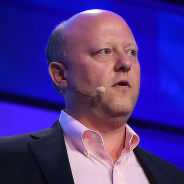 A bald man wearing a pink dress shirt and dark suit jacket speaks at a podium with a headset microphone against a blue backdrop, consistent with Jeremy Allaire, CEO of Circle, discussing the company's expansion of USDC into 40 emerging markets and its planned $400M Tazapay deal.