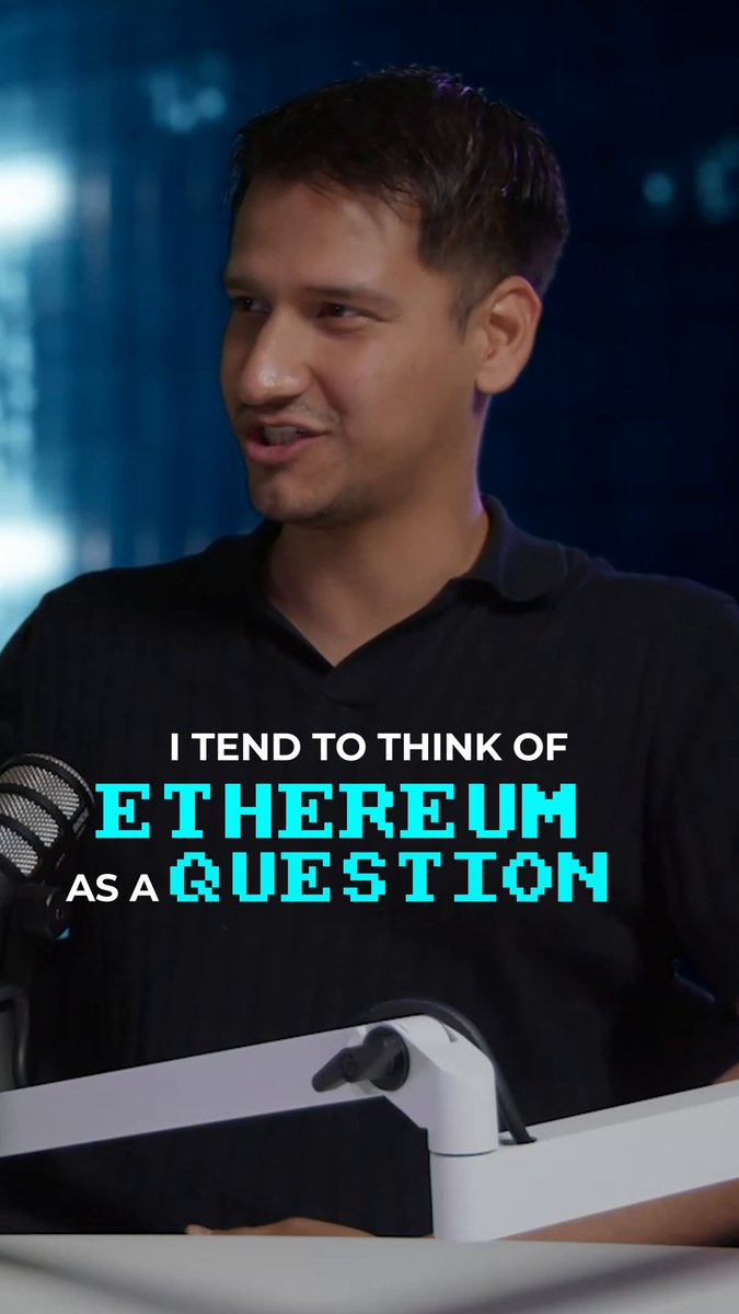 The image features a man wearing a black shirt, standing behind a microphone with a microphone stand. The background of the image has a blue color that contrasts with the man's dark clothing. There are also some words written above him, which seem to be part of an advertisement or promotional material related to cryptocurrency and blockchain technology.