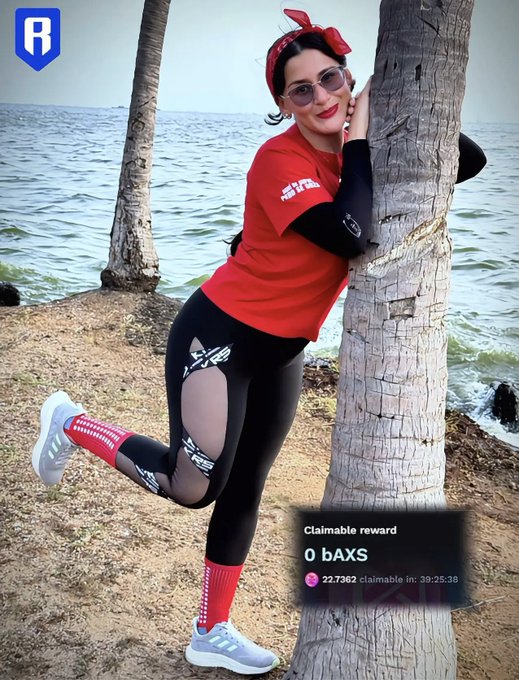 A woman wearing a red headband, sunglasses, a red t-shirt, and black leggings poses against a tree trunk by the water, with a "Claimable reward 0 bAXS" notification visible at the bottom.