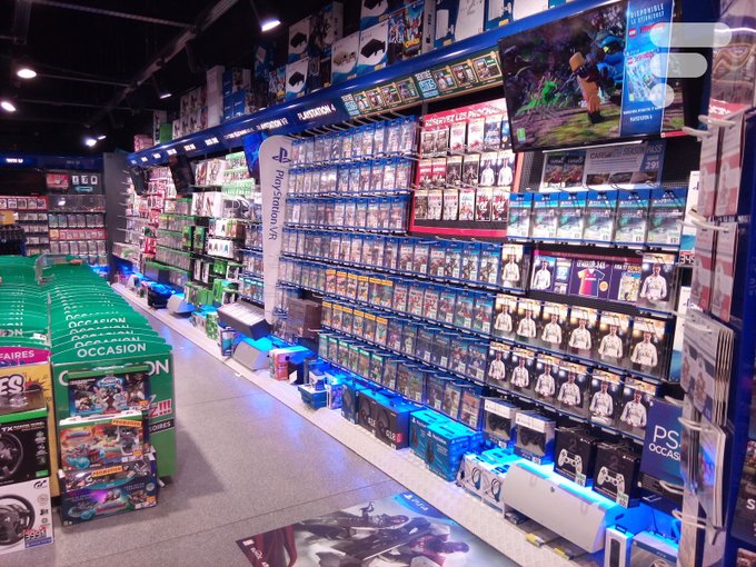 The image shows a retail video game store aisle displaying rows of PS4 and PlayStation titles on shelves, with green "Ocasión" (secondhand) display stands in the foreground and an "Earthbreakers" PSVR game prominently featured on the wall. The connection to the post is ironic or cautionary—physical media like video games serves as a visible example of how businesses phase out tangible products (from cartridges to discs to digital downloads), paralleling the article's argument that banks may similarly eliminate physical cash in favor of centralized digital currency.
