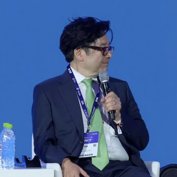 A man in a dark suit and green tie, wearing glasses and a "SPEAKER" lanyard, speaks into a microphone at a conference panel. The image likely depicts Tom Lee, Chairman of Bitmine ($BMNR), discussing the company's recent accumulation of 27,084 ETH toward its 5% ETH treasury goal, in the context of an 8% price drop he described as a "challenging" week.