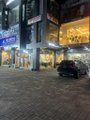 A nighttime city street scene showing a storefront with an 'app' sign and a parked vehicle on a cobblestone road.