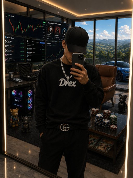 A man wearing a black cap, a black sweatshirt with 'Drex' text, and a chain necklace takes a mirror selfie in a room featuring multiple monitors displaying financial charts and trading data.