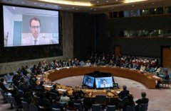 The United Nations Security Council chamber is shown in session with representatives seated around the circular table and a speaker displayed on the screen.