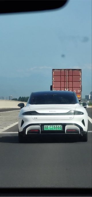 A rear-view shot of a white BYD electric sedan with green Chinese license plate '皖A·CZ4444' driving on a highway, with a red cargo truck visible ahead in the adjacent lane.