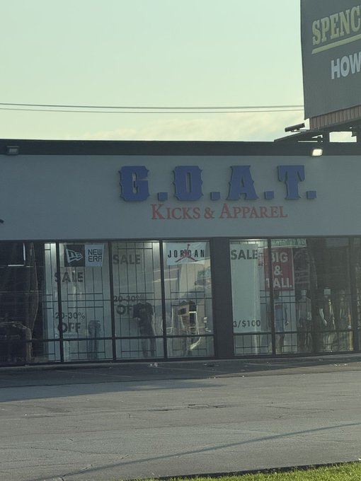 A storefront for 'G.O.A.T. KICKS & APPAREL' with sale signs in the windows advertising 20-30% off, near a Spencer sign.