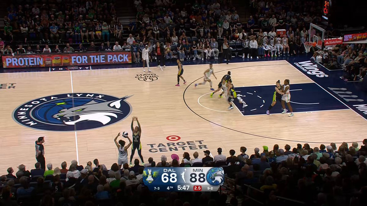 The image shows a basketball game taking place, with players actively engaged in the match. The crowd of spectators can be seen watching intently from various positions around the court. A scoreboard is visible above the court displaying the current score and time remaining for the game. The image also includes some text that reads "Big-time buckets and statement dubs Watch the top plays from last night's Comm Cup action! #WNBA30Season | @coinbase". This suggests that the basketball game might be related to a special event or promotion, possibly tied to the WNBA season.

The image captures an exciting moment in the game as players compete for the ball on the court. The crowd of spectators is engaged and focused on the ongoing match, creating an atmosphere filled with anticipation and excitement.
