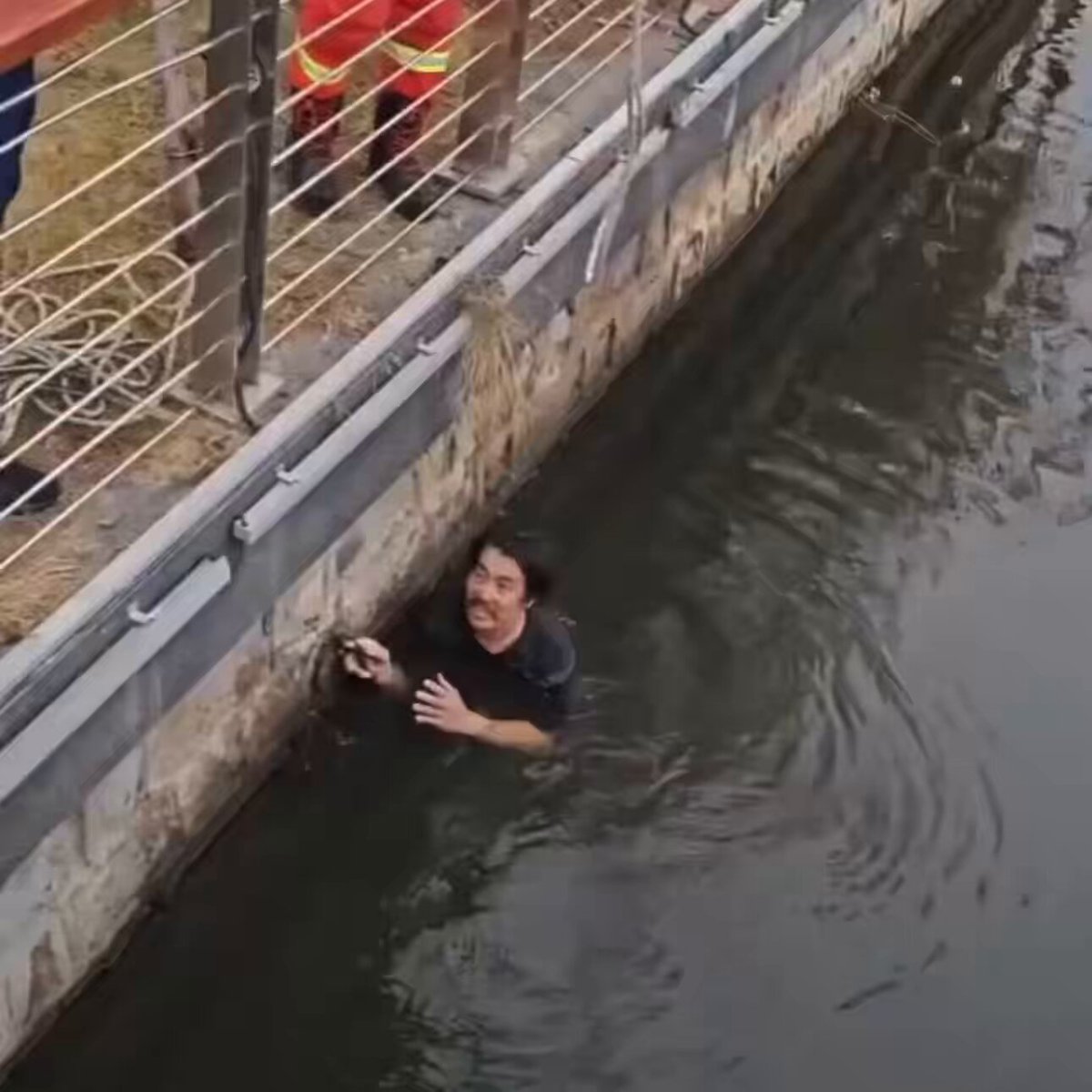 The image shows a man submerged underwater near a concrete wall or barrier, possibly at a waterway with a fence nearby. The caption of the image reads "O people, O crypto community, we won'T sink! We will survive!" This message is related to Bitcoin and cryptocurrency, suggesting that the man's survival might be connected to the digital currency world.