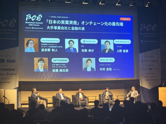 A panel of five speakers sits on stage at the Blockchain Summit 2026 Autumn in Japan, with a large screen displaying the discussion title "「日本の実業資産」オンチェーン化の最先端 大手事業会社と金融の波" (Bringing Japan's Real-World Assets Onchain: The Leading Edge of Corporate and Financial Adoption), featuring panelists from Sony Innovation Fund, Mitsui & Co., Toyota Blockchain Lab, OPTIMISM, and ONIGIRI. The image captures the live discussion that aligns with the post highlighting PacificMeta's APAC tour and the growing convergence of traditional Japanese corporations and financial institutions with blockchain technology.