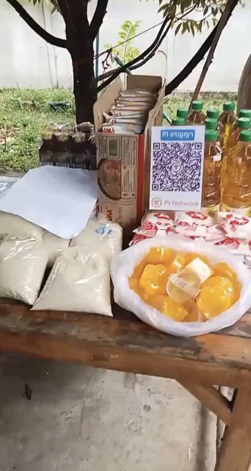 A street vendor's table displays various goods including bags of powders, bottles of yellow liquid, a bowl of oranges, and boxes, with a VietQR QR code for the merchant 'Pt bán giống' visible.