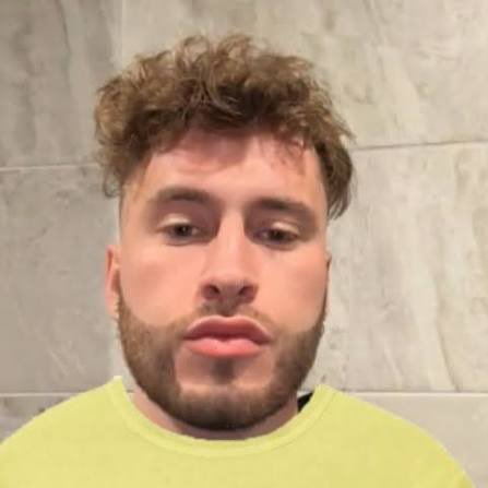A close-up selfie of a young man with curly brown hair and a beard, wearing a yellow shirt against a tiled bathroom wall, accompanying a bio-style post introducing himself as a 19-year-old "mid tweeter deleter + port manager" seeking connections.