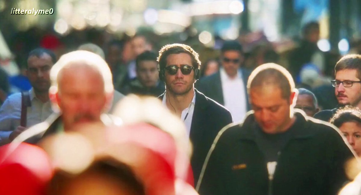 The image shows a man wearing sunglasses, standing among a crowd of people who are also wearing sunglasses. The scene appears to be set in an urban environment with buildings visible in the background. The focus of the image seems to be on the main subject - the man in sunglasses - and it is unclear if there are any other individuals or objects present that could be considered as part of the scene.