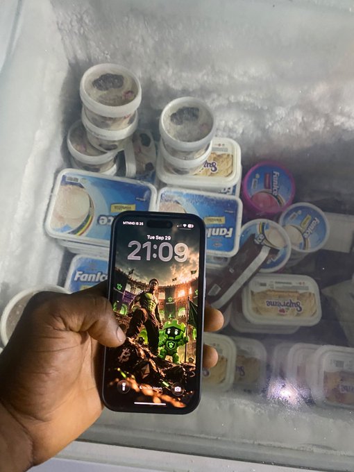 A hand holds a smartphone displaying a lock screen at 21:09 on Tue, Sep 23, featuring a warrior video game character and "Gamdom" branding, while the open freezer behind it is stocked with tubs of FanIce and Supreme ice cream.