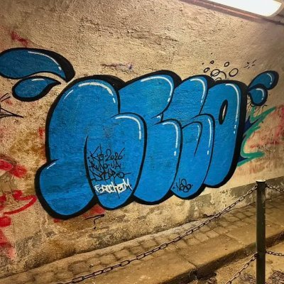 A blue graffiti piece spelling out what appears to be 'GLUE' or similar lettering is spray-painted on a textured concrete wall, with a safety chain visible at the bottom of the image.