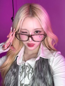 A young woman with blonde hair wearing pink-tinted glasses and a white jacket poses against a bright pink background.