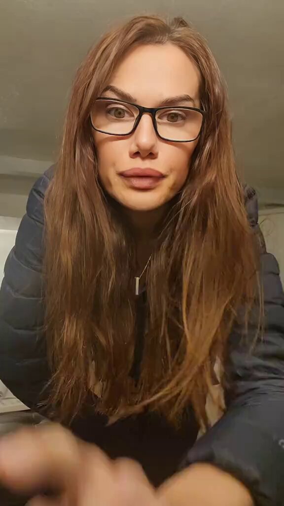 The image features a woman with long brown hair wearing glasses, posing for a picture while looking directly at the camera. She has a serious expression on her face as she looks into the lens. The background appears to be a room or a hallway, but there is no visible text in the image. The focus of the image seems to be on the woman and her facial expression rather than any additional information provided by the post.