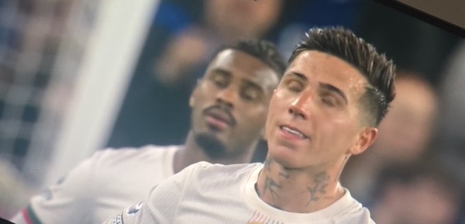 A close-up shows two soccer players in white jerseys, with a tattooed player in the foreground appearing dejected after a play.