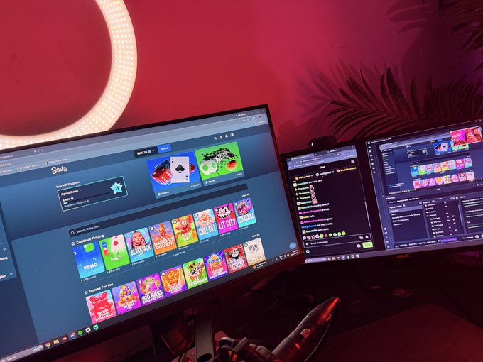 A multi-monitor streaming/gaming setup displays Stake.us casino games alongside streaming software, set in a room with pink ambient lighting and a neon ring light, matching the post's promotion of a live gambling session to win money.