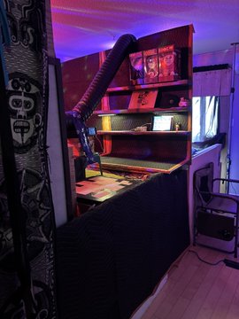 The image shows a room with a black shelf that has a TV mounted on top of it, along with some books and other items. The wall behind the shelf features a large design or pattern, adding an artistic touch to the space. A poster is also displayed in the room, which seems to be related to the post about dog owners built-in holders for their belongings.