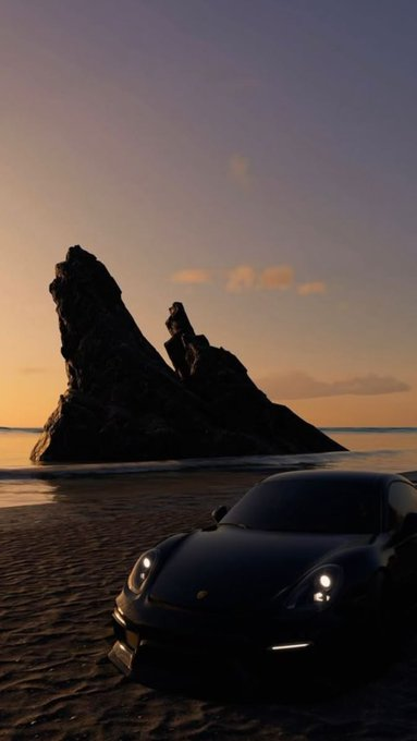 A dark sports car, appearing to be a Porsche, parked on a sandy beach with headlights on, set against a dramatic rocky sea stack silhouetted at sunset.