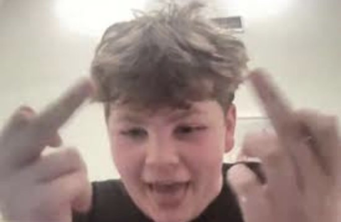 A blurry close-up of a young boy pointing both index fingers at his head with a smiling expression.